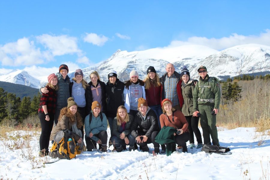 All 12 students, plus Ms. Dooley and Mr. Swanson, take a hike in East Glacier National Park, with beautiful mountains in the background.