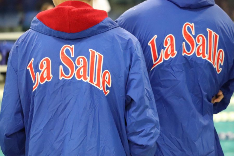 Two swimmers wear their deck coats as they watch their teammates compete.