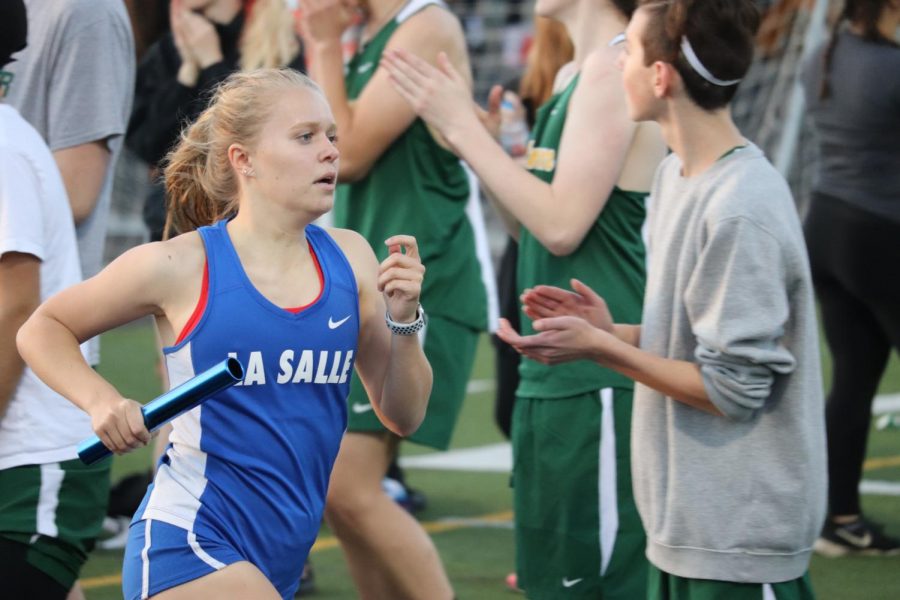 Junior+Evelyn+Bergler+is+cheered+on+by+the+rest+of+the+team+as+she+comes+around+the+corner+for+the+last+straightaway+of+the+4x400+relay.