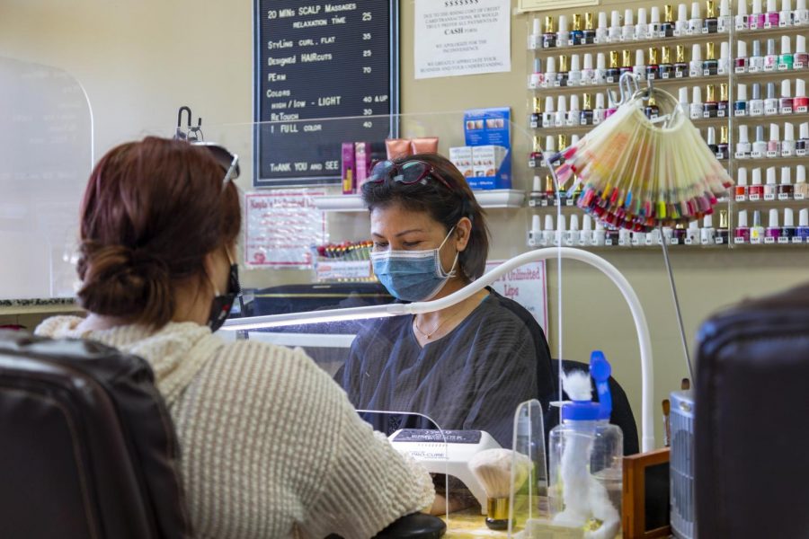 Nails Unlimited store manager Kim Nguyen works behind a clear plastic shield and wears a face mask.